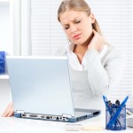 Woman sitting at desk feeling sore neck from looking down at laptop